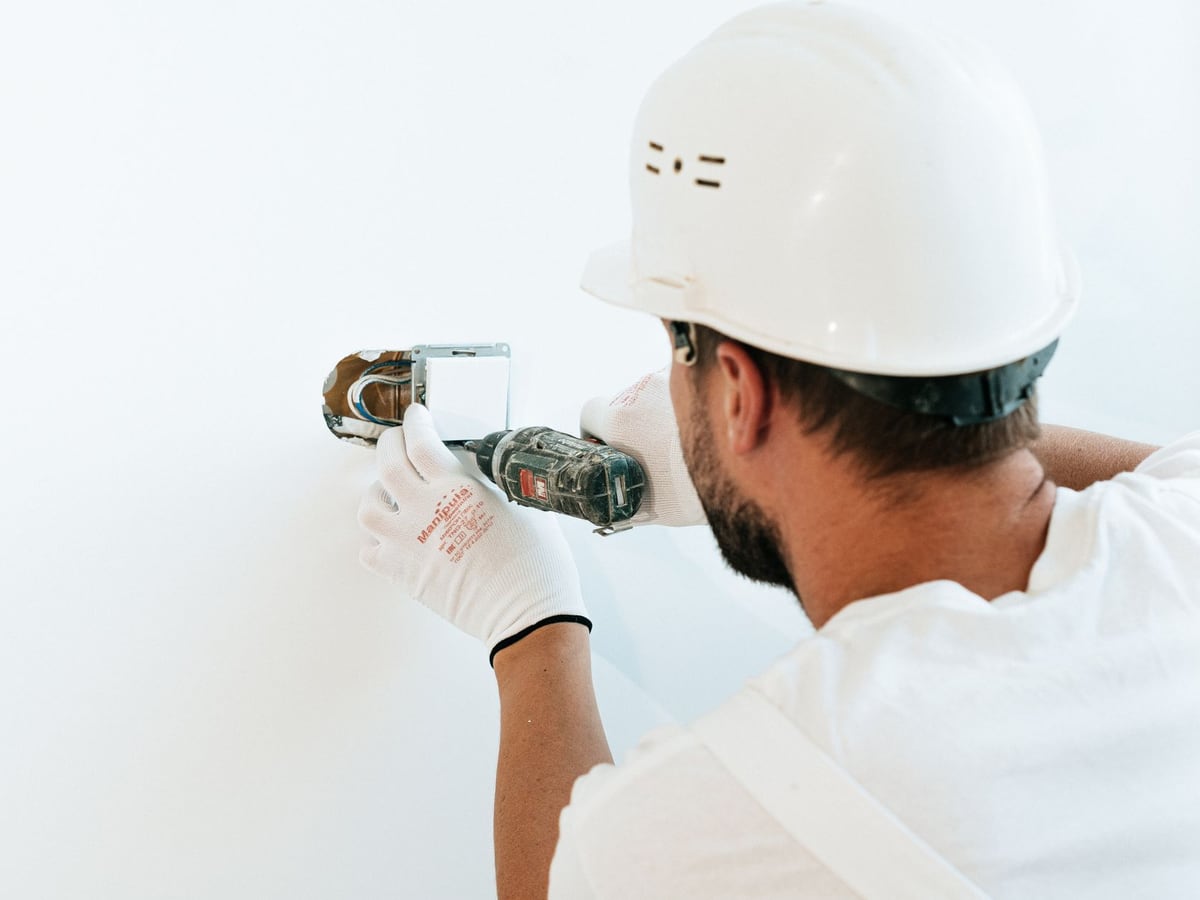 Électricien fixant un mécanisme d'appareillage dans un mur blanc